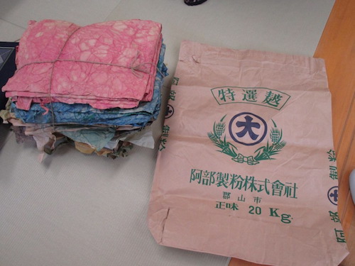 向かって左側には染料加工されて折りたたまれた紙の束。右側には加工前の阿部製粉の飼料袋