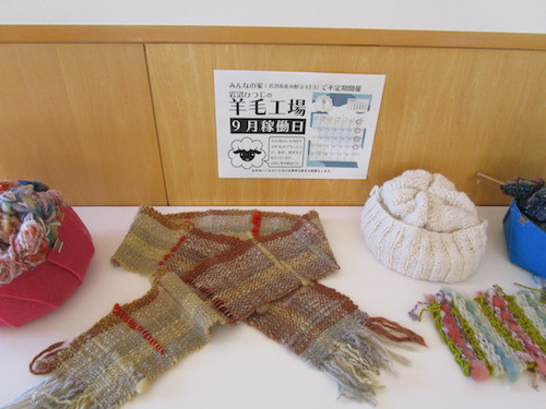 いわぬまひつじ村の羊の毛で編んだマフラーや帽子と、「岩沼ひつじの羊毛工場」の稼働日のポスター