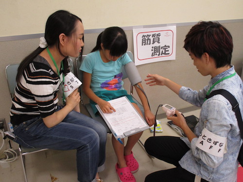 女児の血圧を測定している学生ボランティア二人