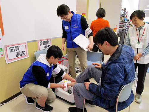 横浜市立大学医学部看護学科の先生で薬剤師のお父さんが見守る中、慣れた手つきで骨密度測定をすすめる中学2年生の若いボランティア、吉田ジュニアです